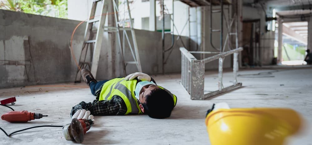 man lying on concrete floor after falling off ladder at a construction site