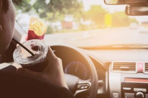 driver operating the vehicle with fries in one hand and drinking out a cup with the other hand, clear signs of a distracted driver