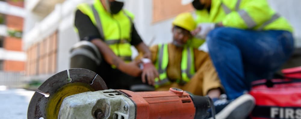 construction worker injured by a circular saw, surrounded by two other employees to apply pressure to the wound on the job site.