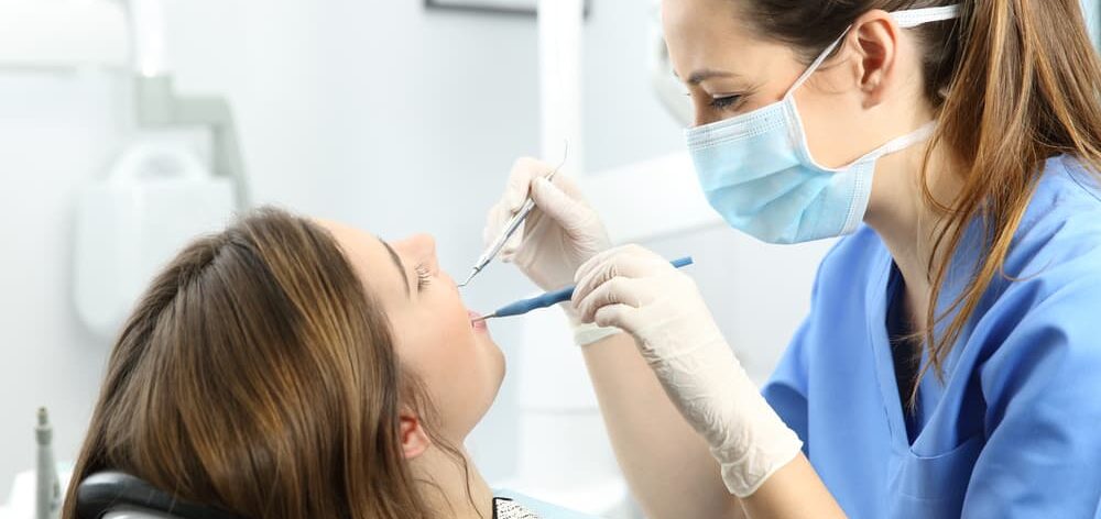 dental hygienist using both hands while cleaning patients teeth; repetitive motion can lead to injuries
