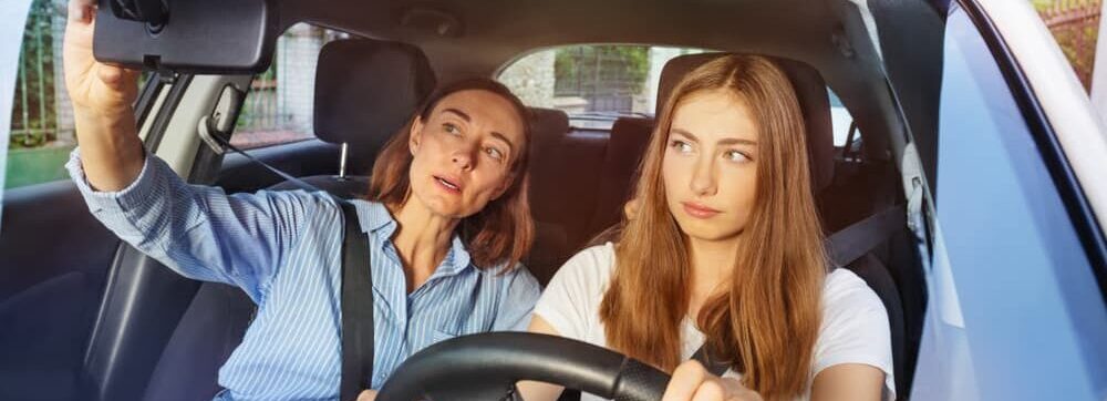 mom and daughter in car; parent teaching teenage driver the use of rearview mirror