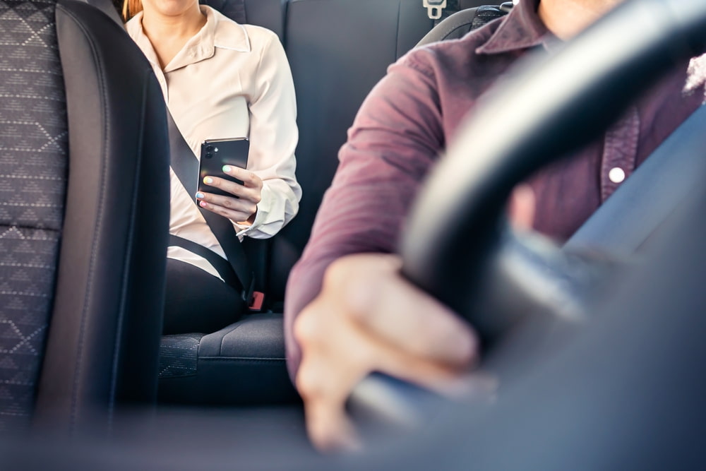 driver transporting passenger who is seated with safety belt on, using the phone