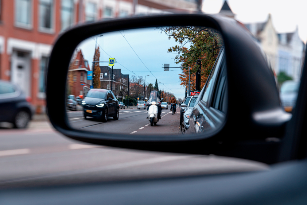 picture of a car's left side rear view mirror which shows a motorcycle following from behind the driver