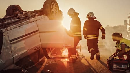 A team of firefighters is positioned next to a flipped car, actively responding to the accident scene.