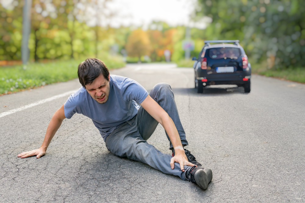 man hit by car, lying down in the road clutching injured leg and car leaving the scene, driving away