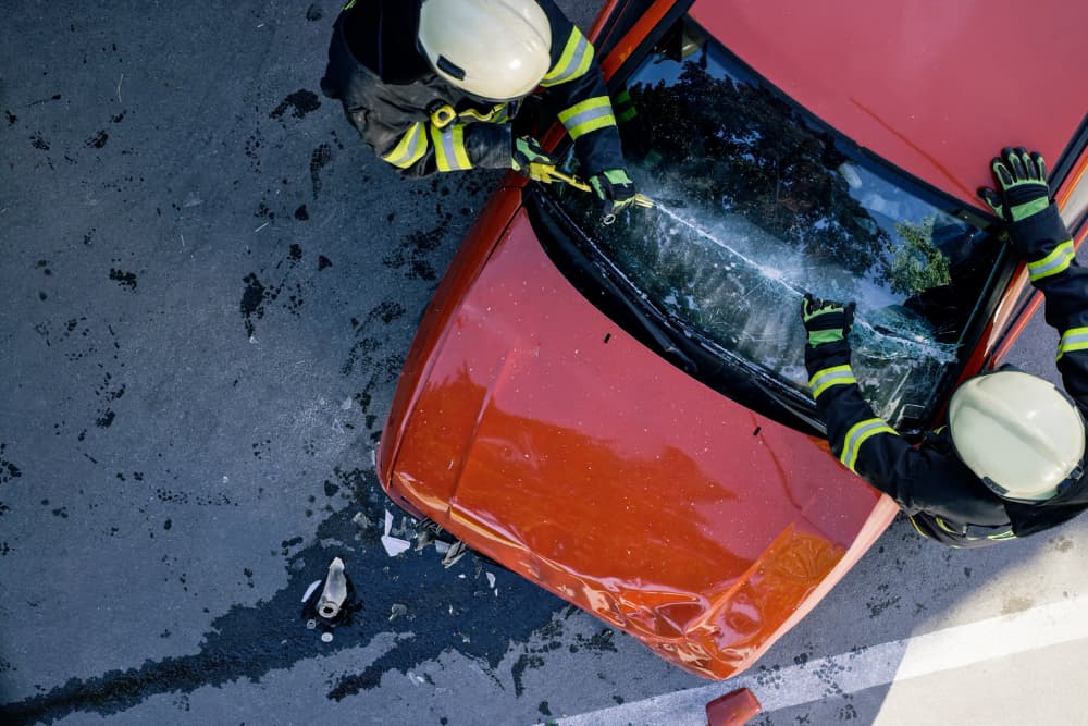 Overhead view of firefighters using a glass cutter to cut car windscreen after accident.